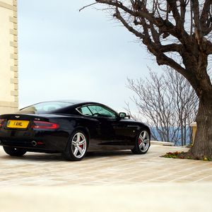 Превью обои aston martin, db9, 2006, черный, вид сбоку, стиль, спорт, астон мартин, авто, здание, дерево, небо