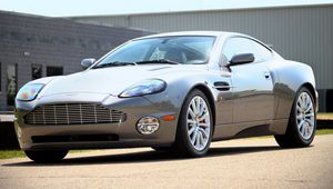 Превью обои aston martin, v12, vanquish, 2001, серый, вид сбоку, стиль, астон мартин, здание