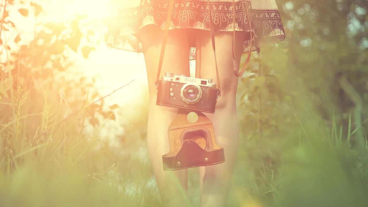 Обои девушка, фотоаппарат, солнце, трава, ноги, платье, блик