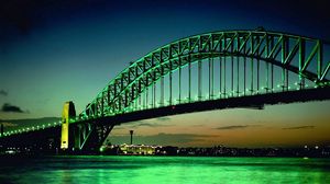 Превью обои мост, большой, зеленый, фон, дуга, огни, вода, ночь, здания, на горизонте, небо, облака, рыже-зеленые