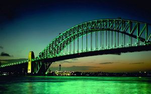 Превью обои мост, большой, зеленый, фон, дуга, огни, вода, ночь, здания, на горизонте, небо, облака, рыже-зеленые