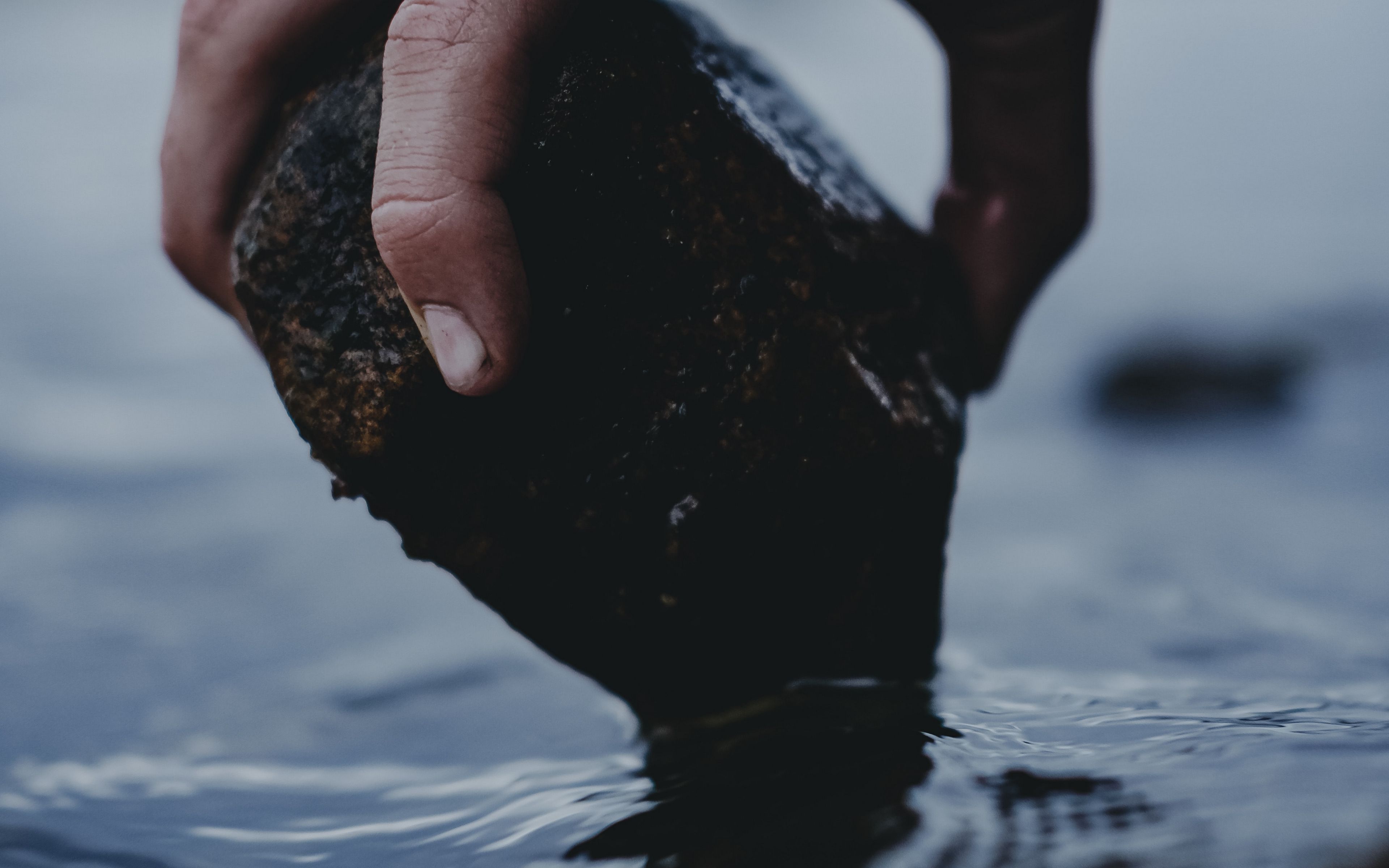 Черная вода далеко. Камешки на ладони. Брошенный камень. Бросание камня в воду. Руки камни вода.