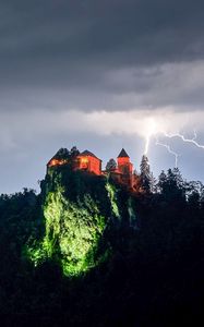 Превью обои скала, дом, свет, молния, сумерки